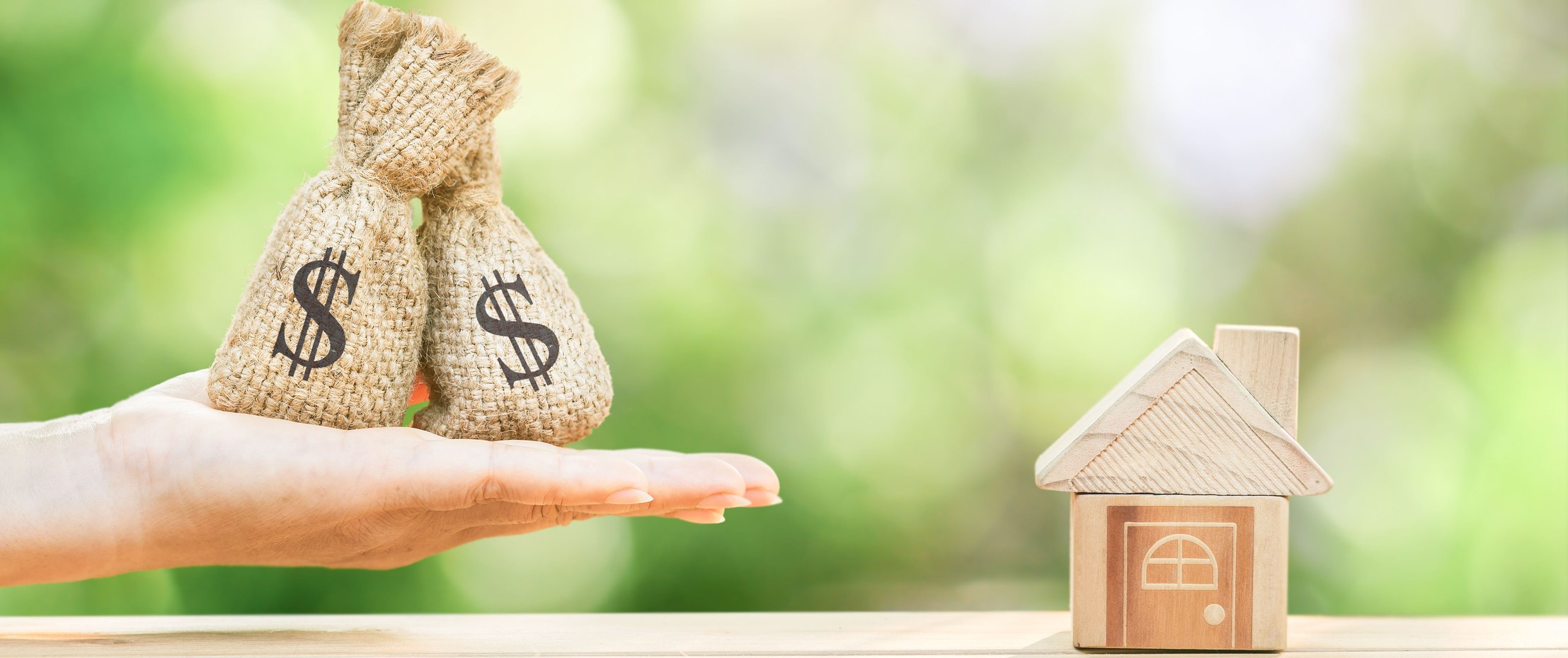 woman holding money bags next to a small wooden house figurine
